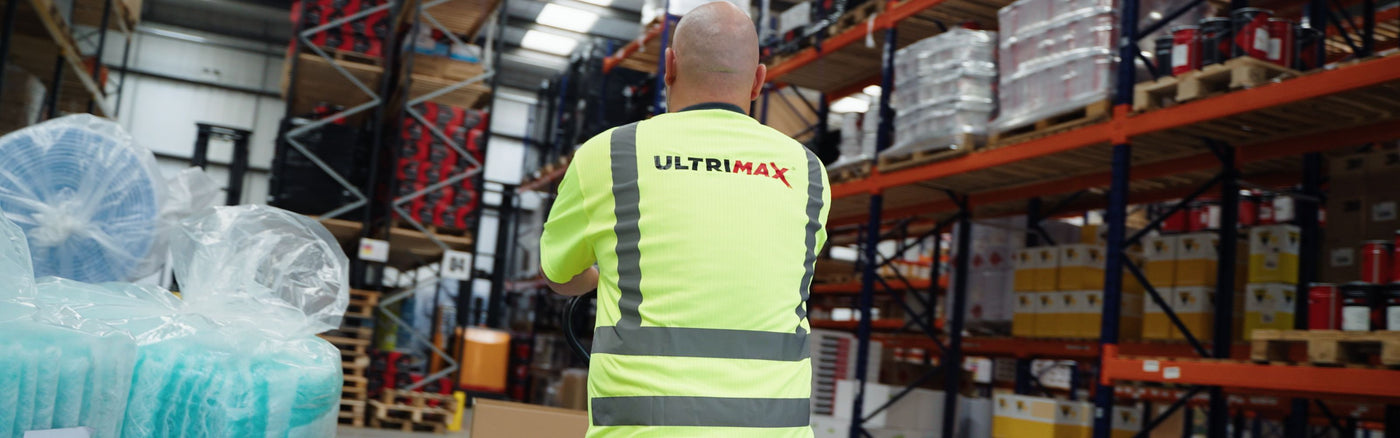 person wearing a high visibility top in a warehouse, pushing a trolley
